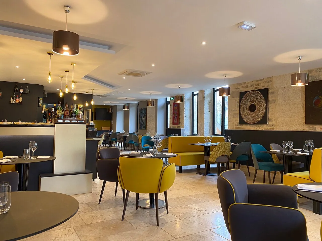 La salle du restaurant Le Point d'Orgue : banquette safran, chaises pétrole et tables dressées, avec le bar en arrière-plan.